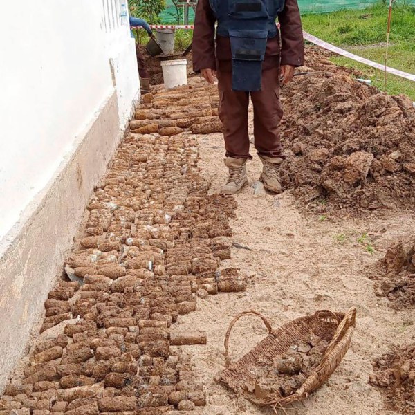 In this photo released by the Cambodia Mine Action Center, CMAC, a diminer expert stands near a pile of unexploded ordnances at Queen Kosamak Hight School in Kratie Province, northeastern of Phnom Penh, Cambodia, Sunday, Aug. 13, 2023. Cambodian authorities have temporarily closed the high school where thousands of pieces of unexploded ordinance from the country's nearly three decades of civil war have been unearthed. (Cambodia Mine Action Center via AP)